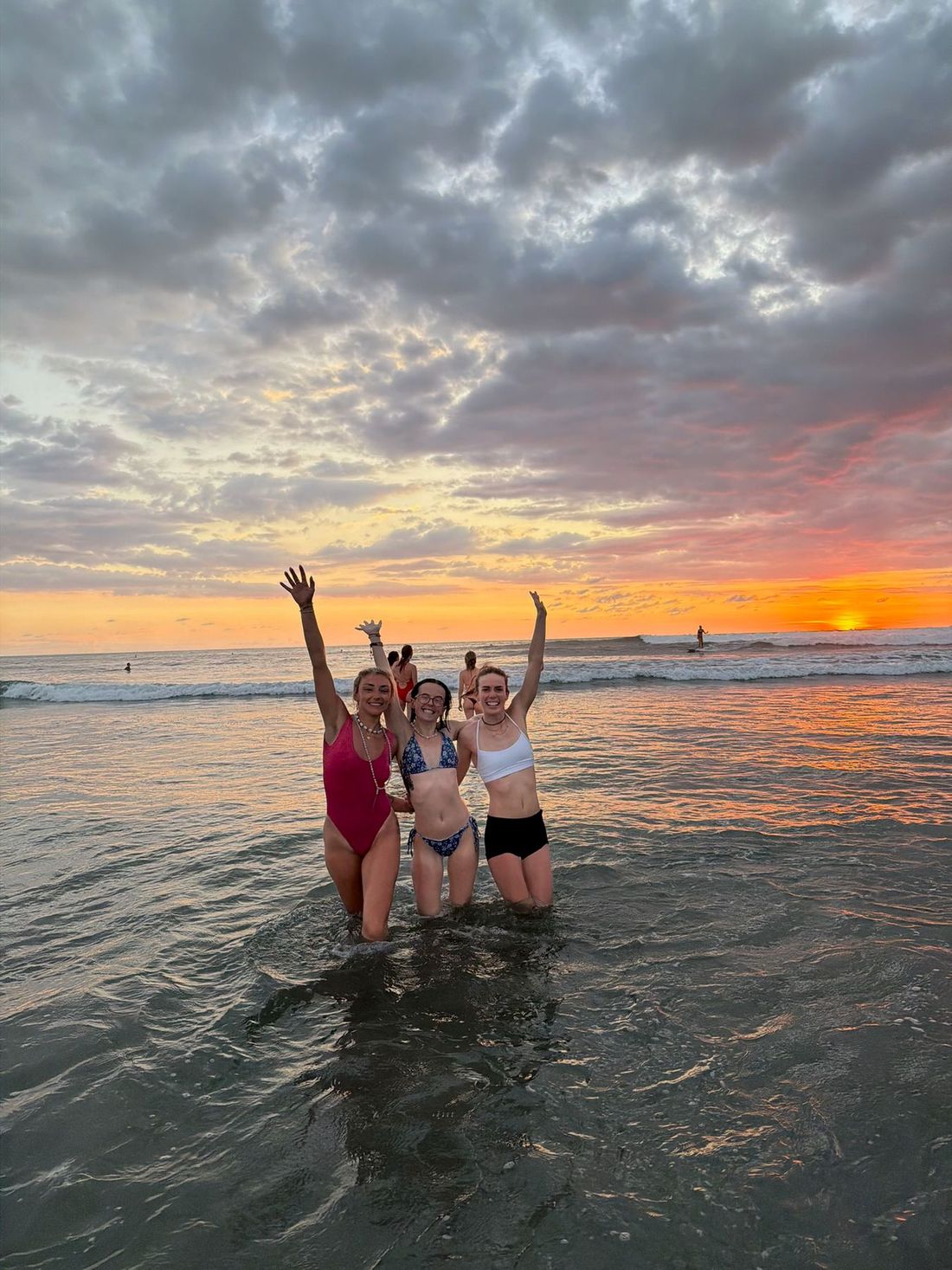 The group standing in the shallows with arms raised as the sun goes down